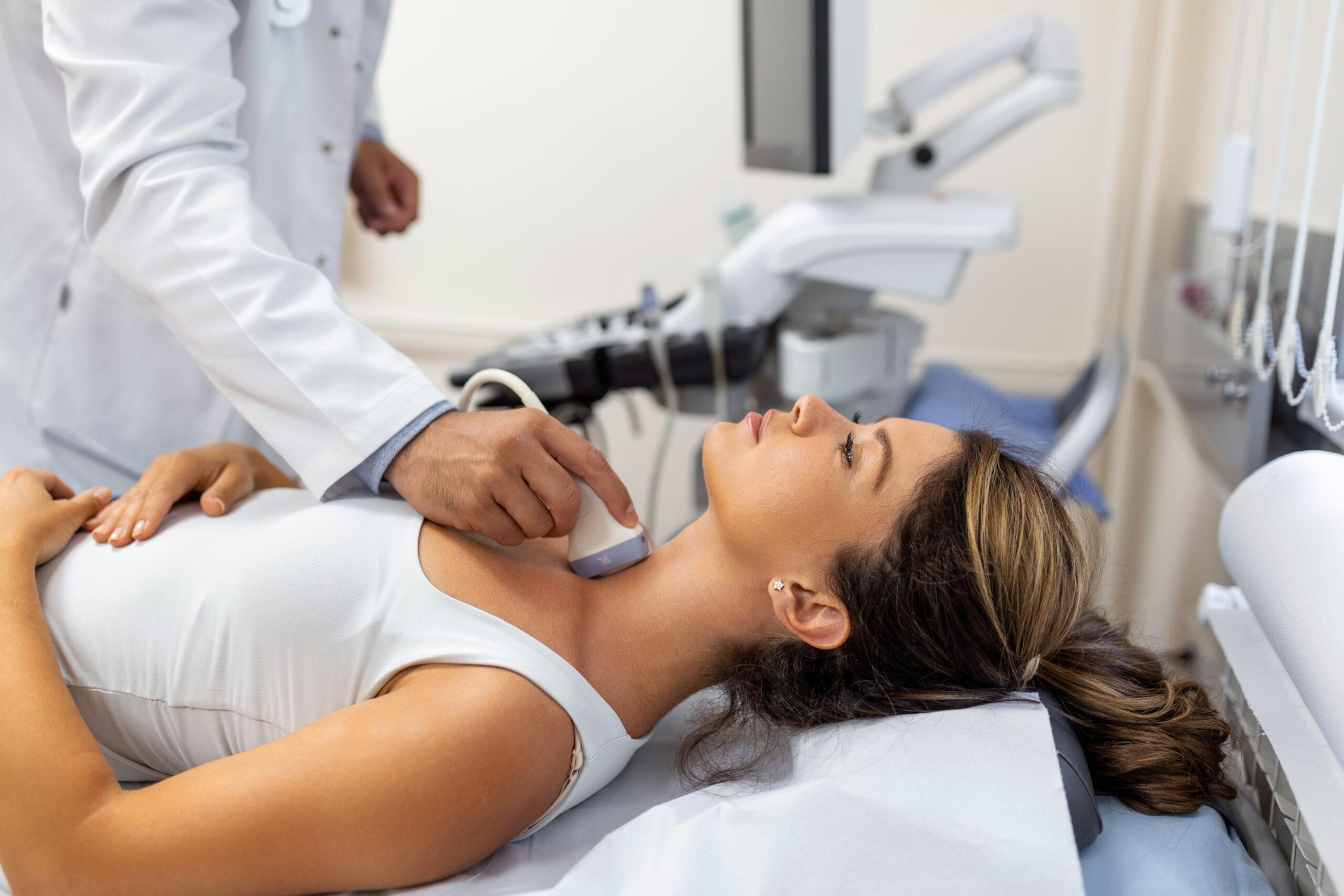Doctor making ultrasound of thyroid gland to woman patient in clinic. Diagnosis and treatment of autoimmune thyroiditis concept Doctor making ultrasound of thyroid gland to woman patient in clinic. Diagnosis and treatment of autoimmune thyroiditis concept